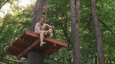 Telefonunu bir ip parkta ağaç üzerinde oturan adam denetler