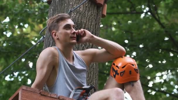 El hombre habla por teléfono sentado en el árbol en un parque de entretenimiento — Vídeo de stock