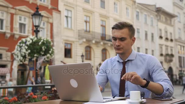 Человек работает с ноутбуком, сидя в кафе на улице — стоковое видео