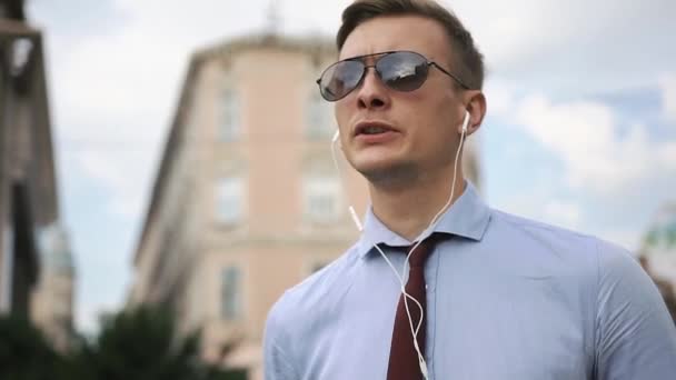 Young man talks via headphones on the street — Stock Video