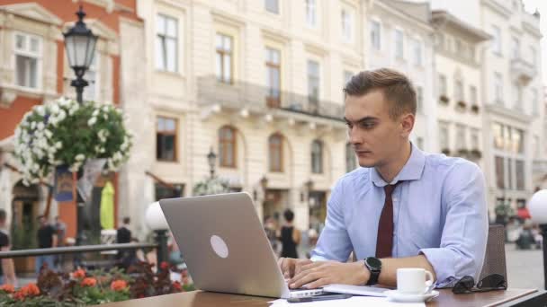 Člověk pracuje s notebookem sedět v kavárně na ulici — Stock video