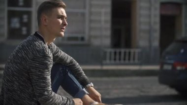 Sokakta oturan genç adam sigara içiyor