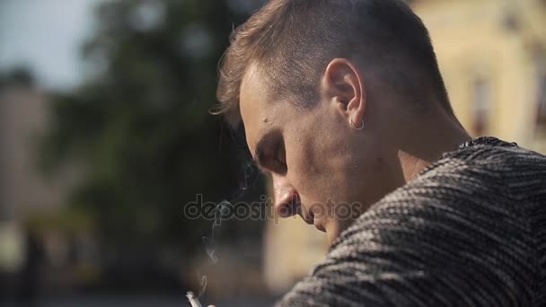 Jonge man rookt zittend op de straat — Stockvideo