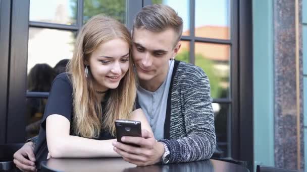 Fiú és lány nézni valamit a telefon, ül egy kávézóban — Stock videók