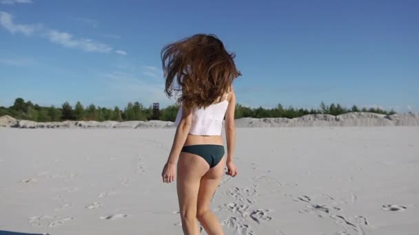 Woman in white top shakes her hair walking on white sand under blue sky — Stock Video