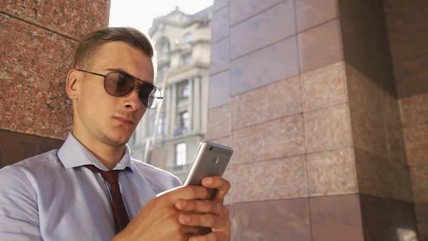 Fiatal ember ellenőrzi a telefon állt az utcán — Stock videók