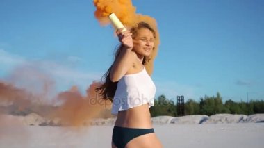 Esmer kadın beyaz üst ve siyah Bikini Turuncu dumanın sahilde çalış.