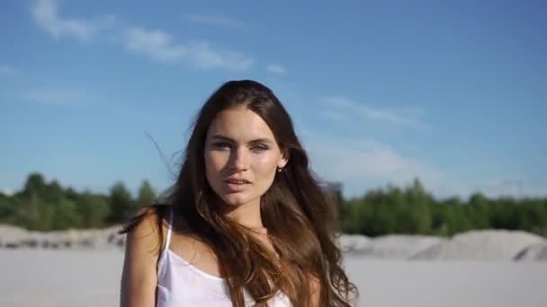 Жінка з довгим волоссям весело танцює на піску під блакитним небом — стокове відео