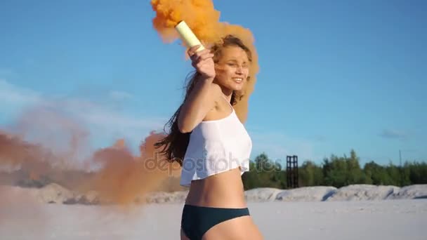 Brunette femme en haut blanc et bikini noir joue avec la fumée orange sur la plage — Video