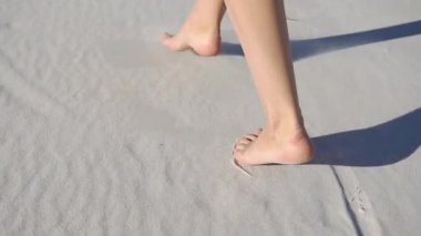 Yalınayak kadın güneşli bir günde beyaz kum üzerinde yürüyor