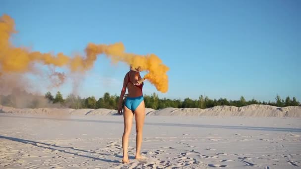 Mujer morena en traje de baño azul juega con humo naranja en la playa — Vídeo de stock