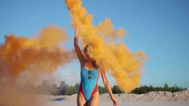 Mujer morena en traje de baño azul juega con humo naranja en la playa — Vídeo de stock