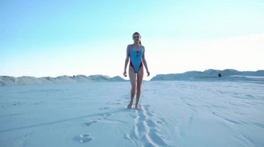 Uzun saçlı esmer kız beyaz kum üzerinde mavi Yüzme elbiseli poz veriyor