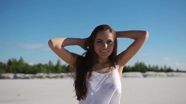 Женщина с длинными волосами весело танцует на песке под голубым небом — стоковое видео