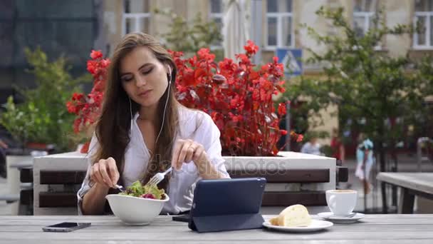 Morena dama escucha la música mientras se sienta en el restaurante antes de que las flores rojas — Vídeo de stock