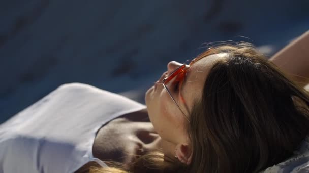 Güneşin altında beyaz kum üzerinde beyaz üst ve kırmızı güneş gözlüğü muhteşem bir kadın yatıyor — Stok video