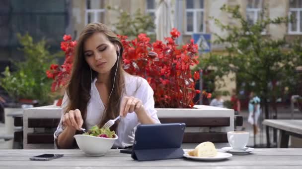 Morena senhora ouve a música enquanto ela se senta no restaurante antes de flores vermelhas — Vídeo de Stock