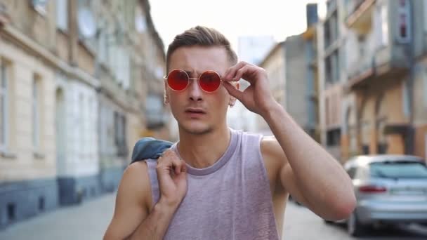 Man in rode zonnebril neemt op zijn jeans jasje wandelen langs de straat — Stockvideo