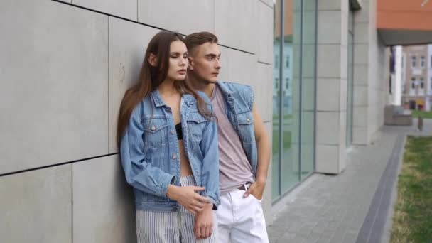 Hombre y mujer vestidos con estilo callejero casual posan ante una pared gris — Vídeos de Stock