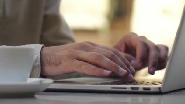 El hombre escribe algo en su portátil sentado en la mesa en la cafetería — Vídeos de Stock