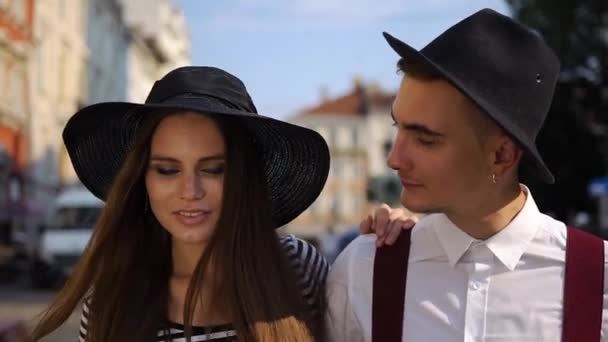 Charming man and woman in black hats walk along the street on the sunset — Stock Video