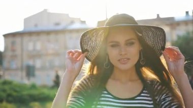 Uzun saçlı, siyah şapka ile muhteşem Bayan cadde boyunca günbatımı üzerinde yürür.