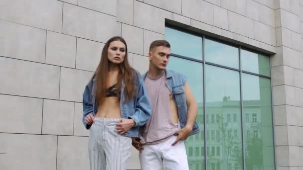 Mężczyzna i Kobieta, ubrana w ułożenia casual styl ulicy przed szare ściany — Wideo stockowe