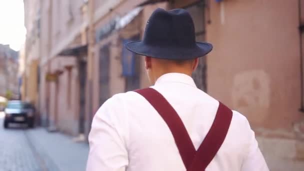 Посмотрите сзади на человека в черной шляпе, идущего по улице — стоковое видео