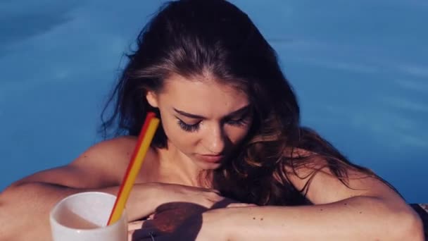 Close up young beautiful girl in swim wear leaning on the edge of a swimming pool and looking at the camera — Stock Video