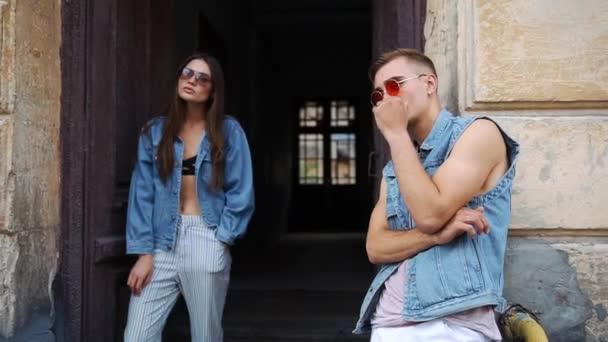 Man och kvinna klädd i casual street stil med solglasögon pose innan en gammal dörr utanför på gatan — Stockvideo
