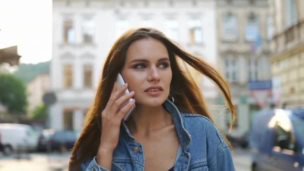 Mulher morena com cabelos longos fala ao telefone enquanto caminha pela rua — Vídeo de Stock