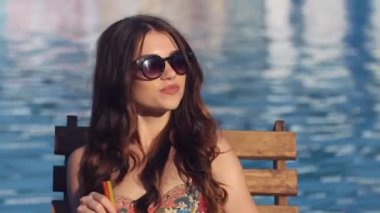 Havuz kenarında oturan ve güneşlenme kokteyl, içme bikini giyen güzel genç kadın kadar kapatın