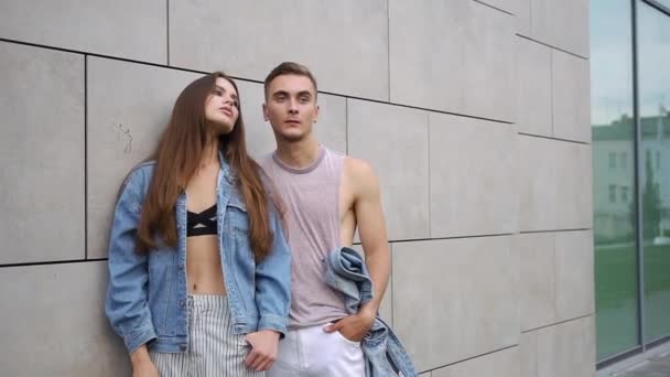 Hombre y mujer vestidos con estilo callejero casual posan ante una pared gris — Vídeo de stock