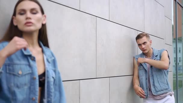 Jongen, gekleed in een roze shirt staat achter een verleidelijke vrouw in jeans jasje — Stockvideo