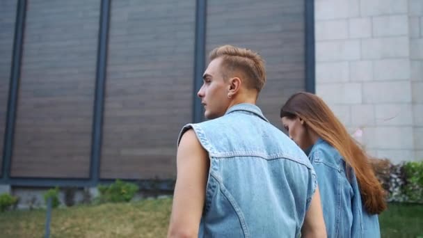 Посмотрите сзади на мужчину и женщину в джинсовых куртках, идущих по улице — стоковое видео