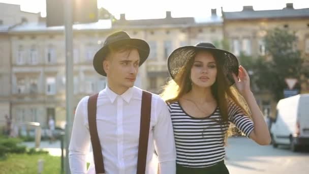 Charming man and woman in black hats walk along the street on the sunset — Stock Video