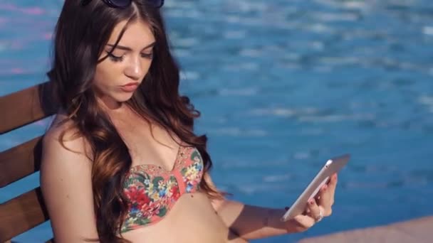 Schöne Mädchen mit einem Tablet und Sonnenbräune in der Nähe des Pools. sie trinkt einen Cocktail — Stockvideo