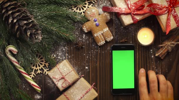 クリスマスの中で横になっている緑の画面でスマート フォンを上から見てください。 — ストック動画