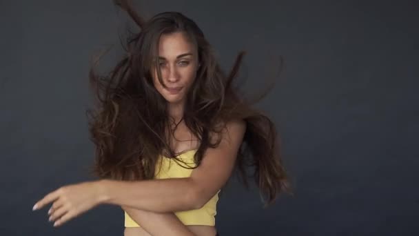 Mujer con top amarillo sacude su largo cabello castaño y baila contra el viento en reversa — Vídeos de Stock