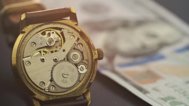 Close-up van uurwerk in een stijlvol horloge dat ligt op honderd dollar biljet — Stockvideo