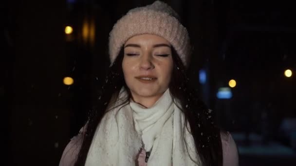 Όμορφη ελκυστική κοπέλα είναι το περπάτημα γύρω από το βράδυ δίπλα σε ένα παράθυρο κατάστημα διακοσμημένα με φώτα Χριστούγεννα και κοιτώντας την κάμερα. Εγκαινιάζει ένα φιλί αέρα. Αργή κίνηση — Αρχείο Βίντεο