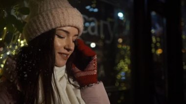 Güzel çekici kız bir window-shop ayakta çelenk ile dekore edilmiş ve ve telefonla konuşuyor. Yeni yıl Noel. Akşam silah, yakın çekim
