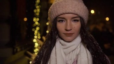 Çelenk ile dekore edilmiş ve kameraya bakarak vitrinler, yakınındaki sokakta yürürken güzel çekici kız. Yeni yıl Noel. Akşam çekim