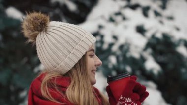 Noel ağaçları karda sıcak içecek kağıt bardak içme yakın duran sıcak giysiler içindeki genç güzel kız içinde. Ağır çekim. Yakın çekim