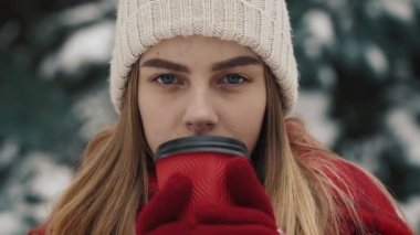 Noel ağaçları karda sıcak içecek kağıt bardak içme yakın duran sıcak giysiler içindeki genç güzel kız içinde. Ağır çekim. Yakın çekim