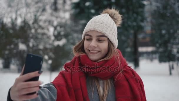 Beutiful Young Girl en el bosque nevado hace una selfie. En cámara lenta. Retrato de la joven y elegante hermosa chica en un parque de invierno — Vídeos de Stock