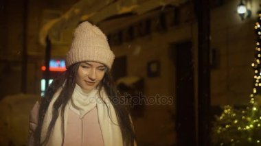 Karlı havalarda şehrin sokaklarında akşam güzel çekici kız gider. Kız şehirde akşam yürüyor. Ağır çekim, kar yağışı