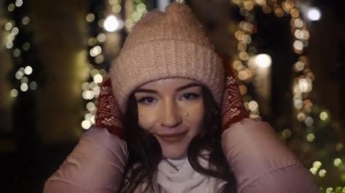 Güzel çekici kız bir window-shop ayakta bir şapka giymiş çelenk ile dekore edilmiş ve kameraya bakıp. Yeni yıl Noel. Akşam çekim
