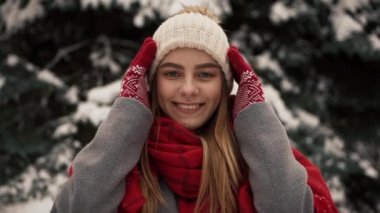 Noel ağaçları duran, bir şapka giymiş ve kameraya doğru seyir sıcak giysiler içindeki genç güzel kız içinde. Ağır çekim. Bir kış parkta şık genç güzel kız portresi