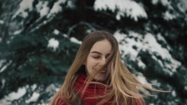 Kafasını sallayarak uzun saçlı Noel ağaçları duran sıcak giysiler içinde güzel bir genç kız, yakın çekim. Ağır çekim